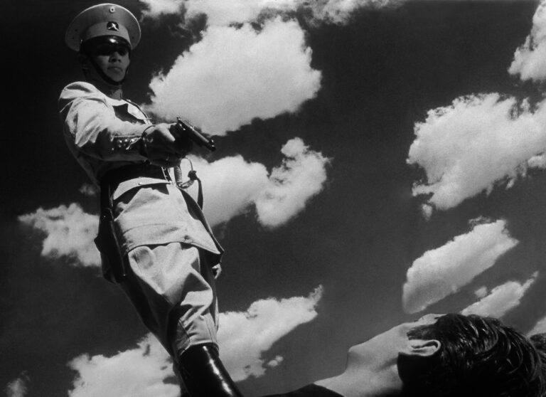 Imagen Blanco y Negro de un militar señalando con una pistola y con el cielo de fondo. Imagen Blanco y Negro.